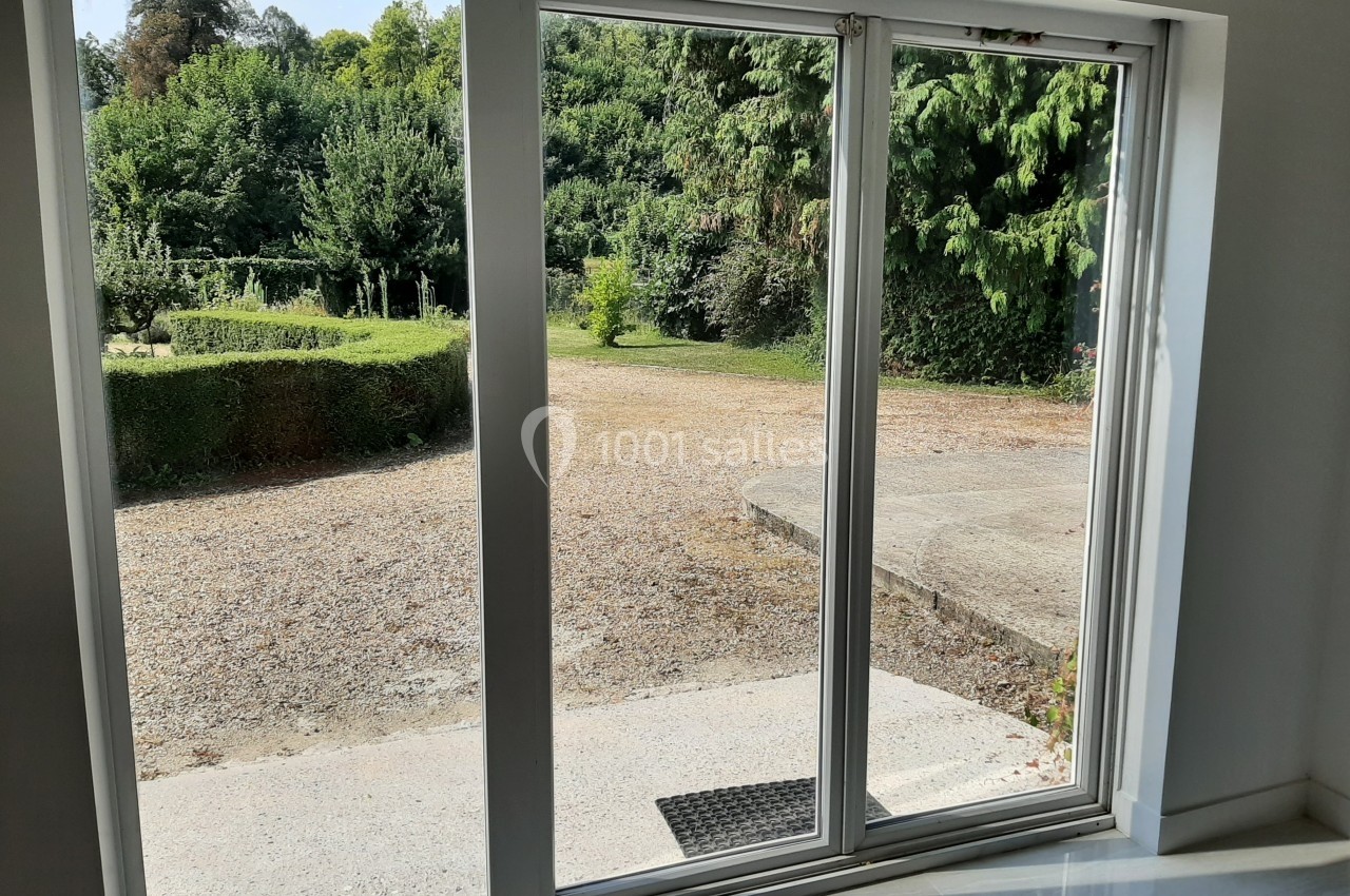 Baie vitrée ouverte donnant sur un jardin verdoyant avec allée gravillonnée et haies taillées.