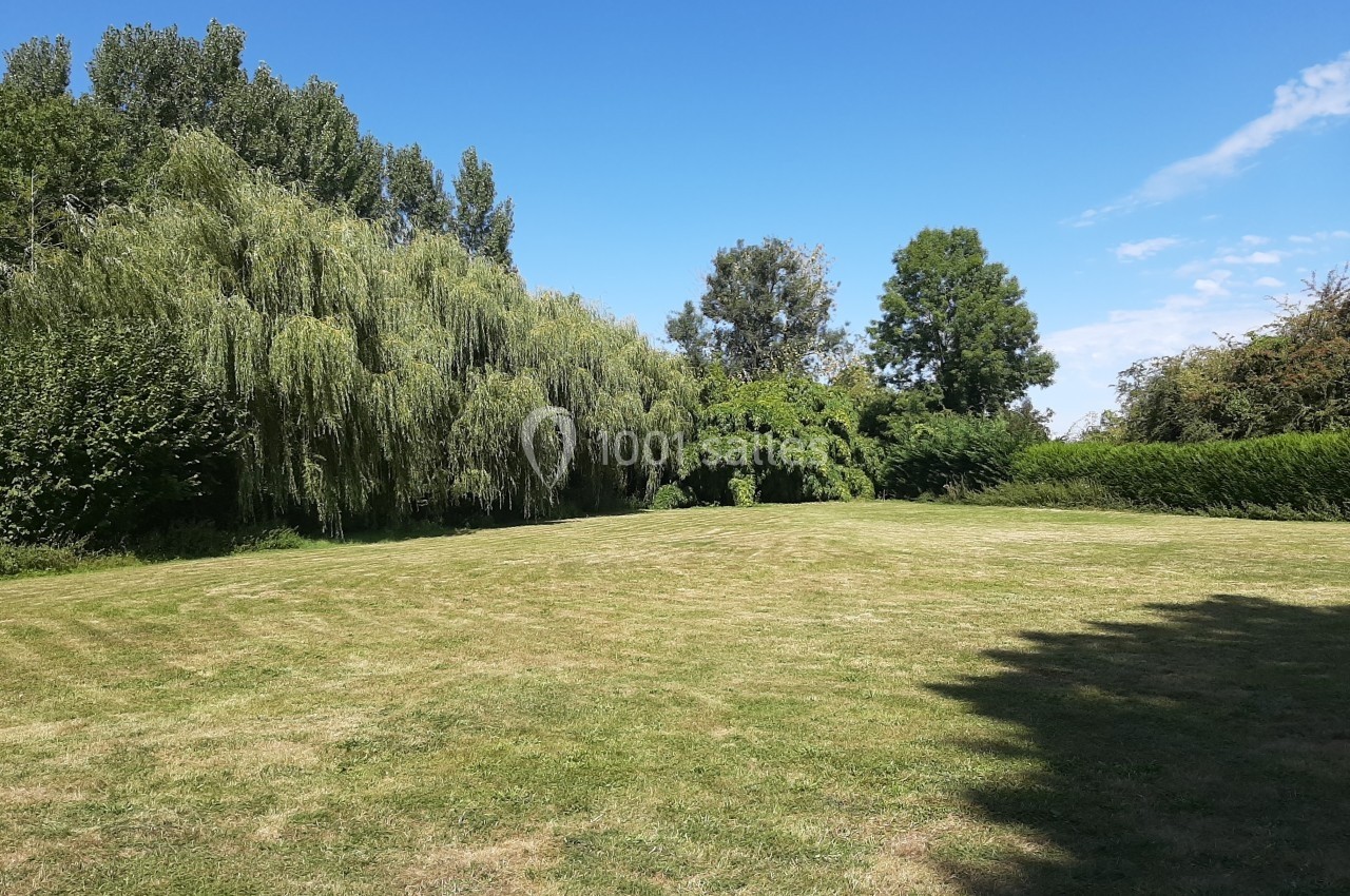 Une pelouse verte entourée d'arbres et de haies sous un ciel bleu dégagé.