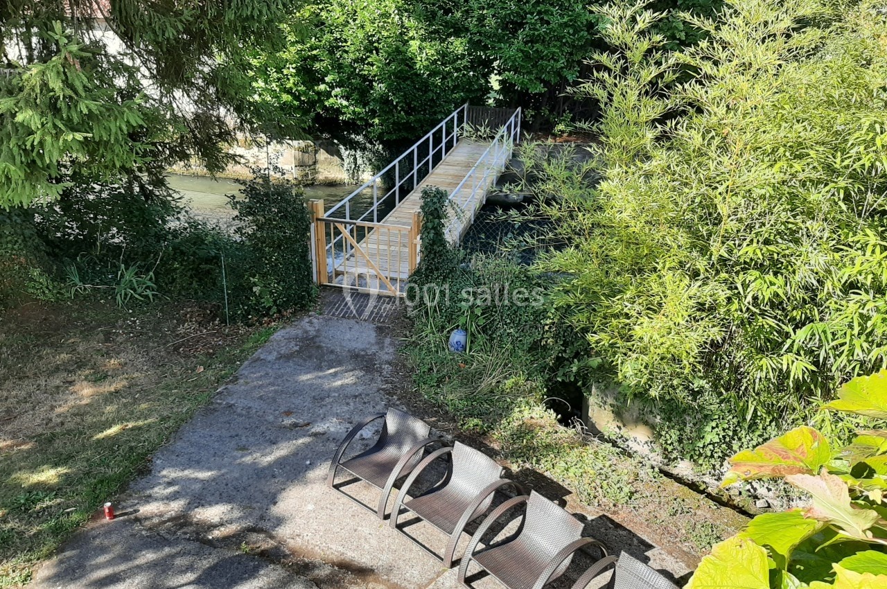 Passerelle en bois et métal traversant un cours d'eau, entourée de végétation, avec des bancs en premier plan.
