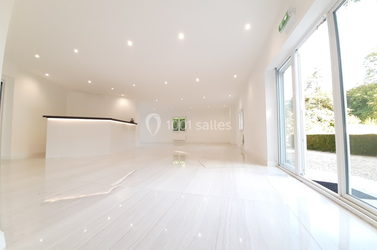Salle lumineuse avec sol en marbre, comptoir moderne, éclairage encastré et grandes baies vitrées donnant sur un jardin.