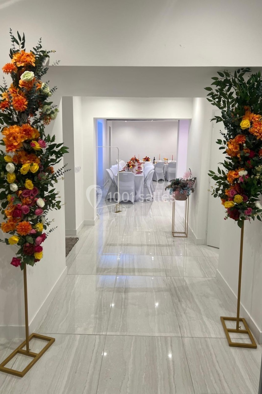 Deux colonnes de fleurs colorées encadrent l'entrée d'une salle lumineuse décorée pour un événement.