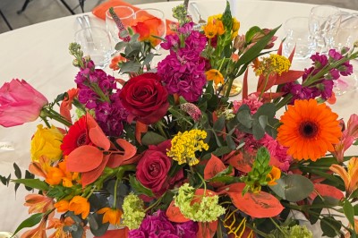 Centre de table floral coloré avec des roses et des verres disposés sur une nappe blanche, bougie en arrière-plan.