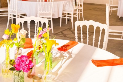 Salle de réception décorée pour un mariage, avec tables dressées, chandeliers suspendus et poutres apparentes au plafond.