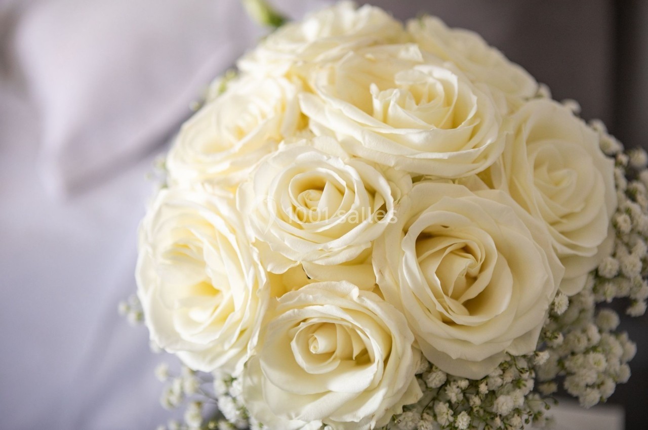 Bouquet de roses blanches entouré de petites fleurs blanches sur un fond flou.