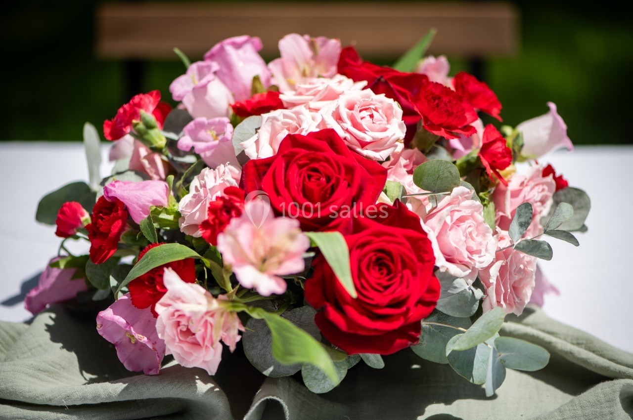 Bouquet de fleurs composé de roses rouges, roses pâles et feuillage vert, posé sur une table blanche.