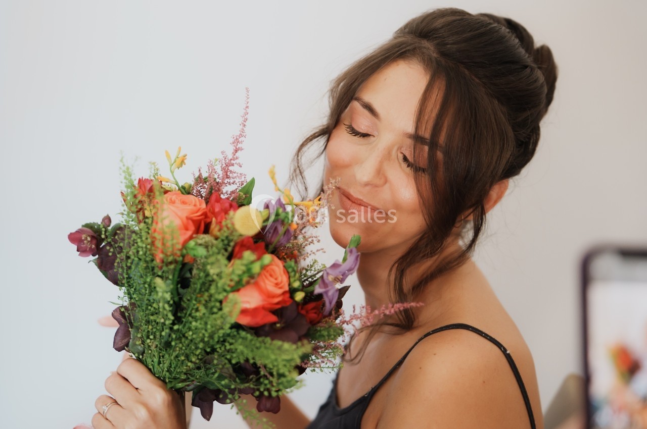 Femme souriante tenant un bouquet de fleurs colorées devant un fond clair.