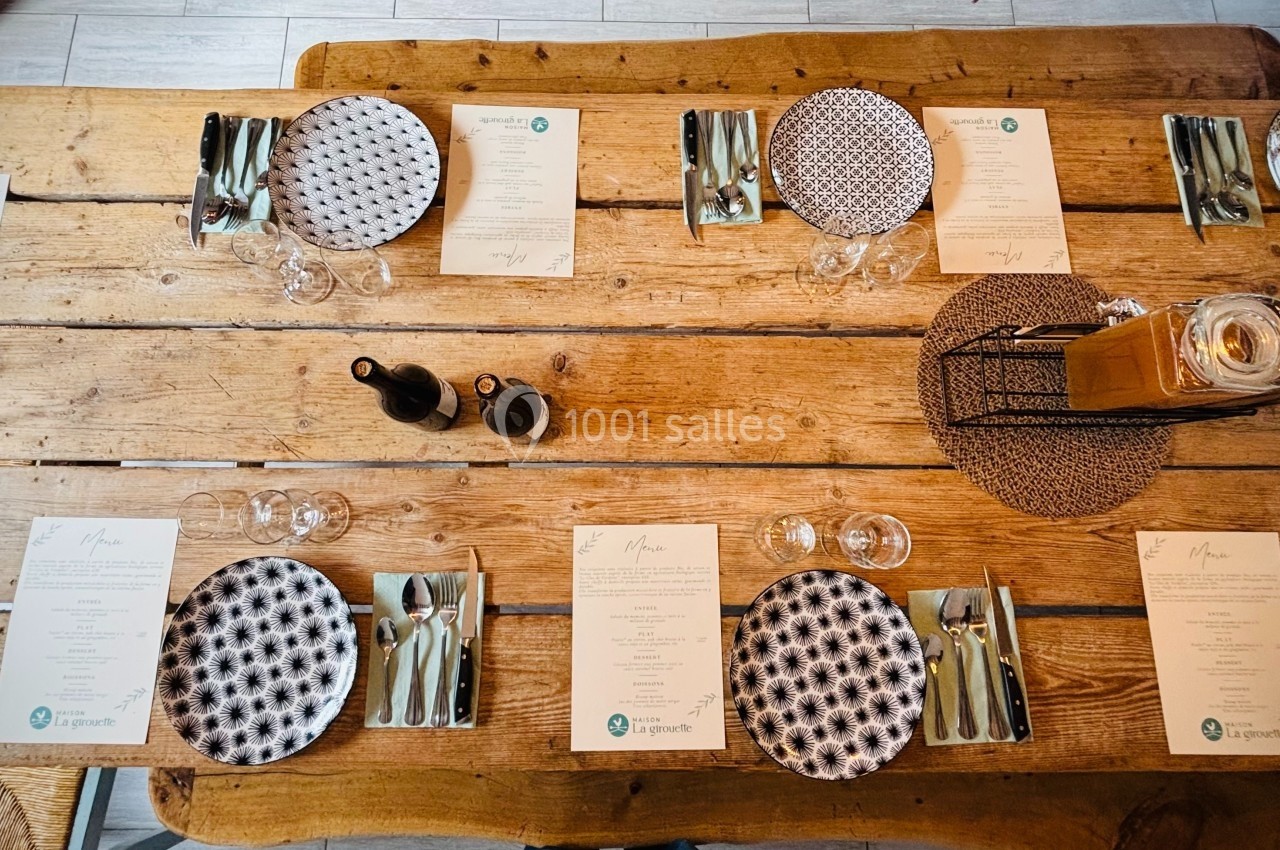 Table en bois dressée avec des assiettes à motifs, couverts, verres, menus et un centre de table décoratif.