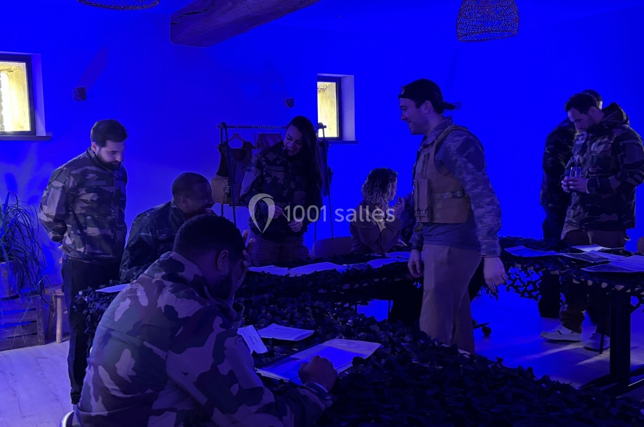 Des personnes en tenue militaire participent à une activité de groupe dans une pièce éclairée par une lumière bleue.