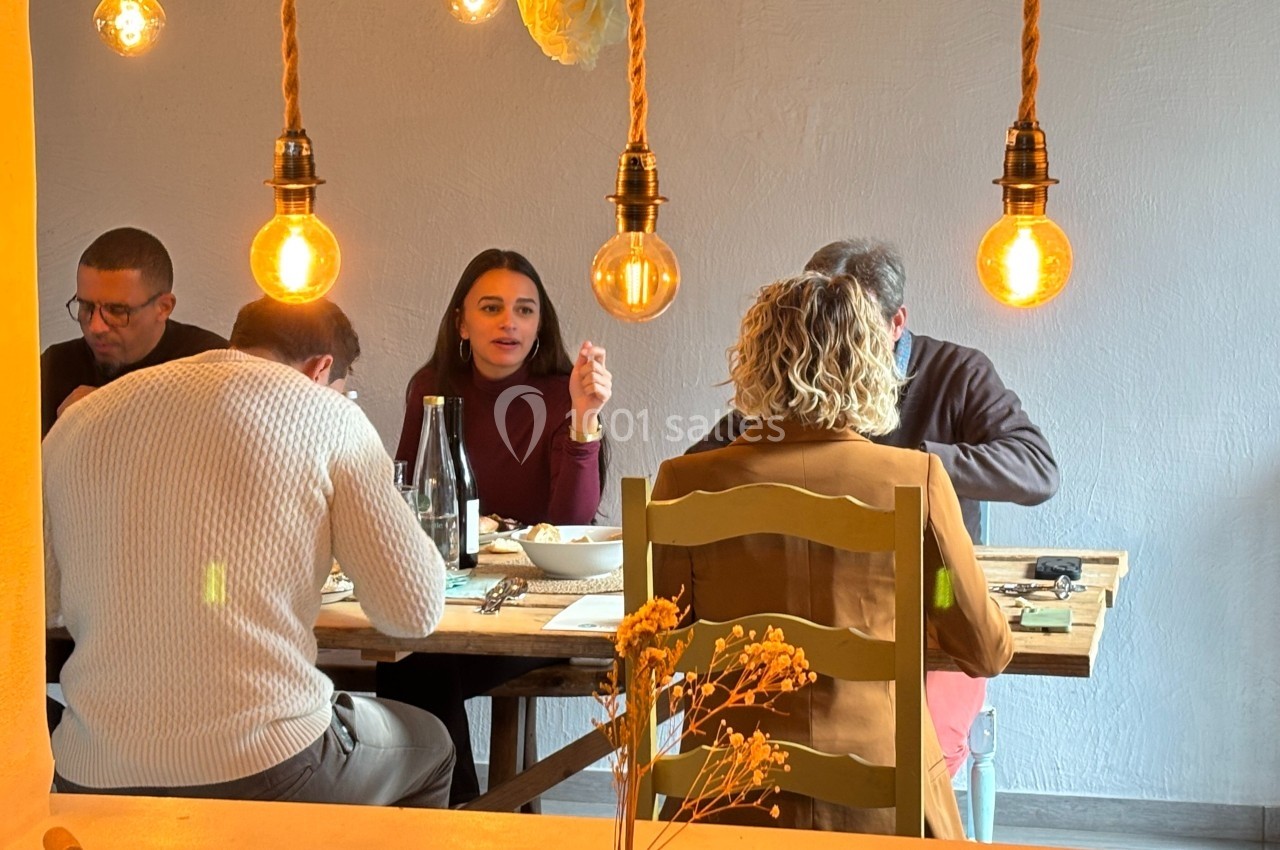 Quatre personnes discutent autour d'une table dans un restaurant éclairé par des ampoules suspendues.