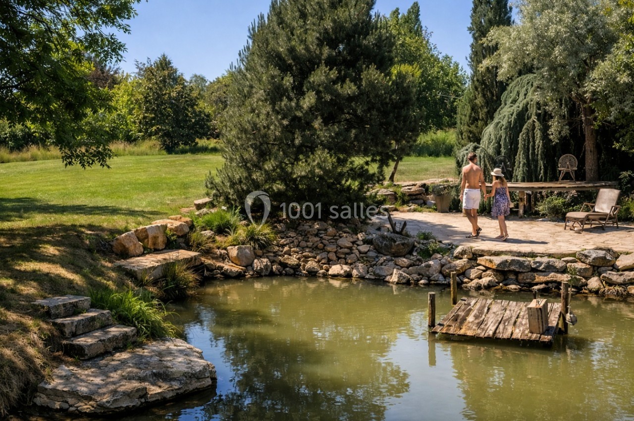 Un homme et une enfant marchent près d'un étang entouré de verdure et de pierres dans un jardin paisible.