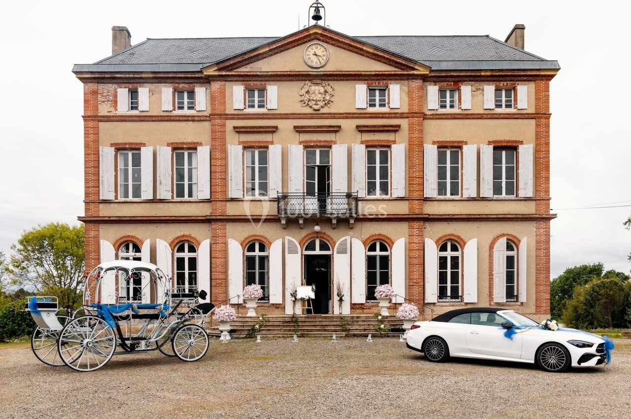 Façade d'un château en briques rouges avec une calèche et une voiture blanche stationnées devant.