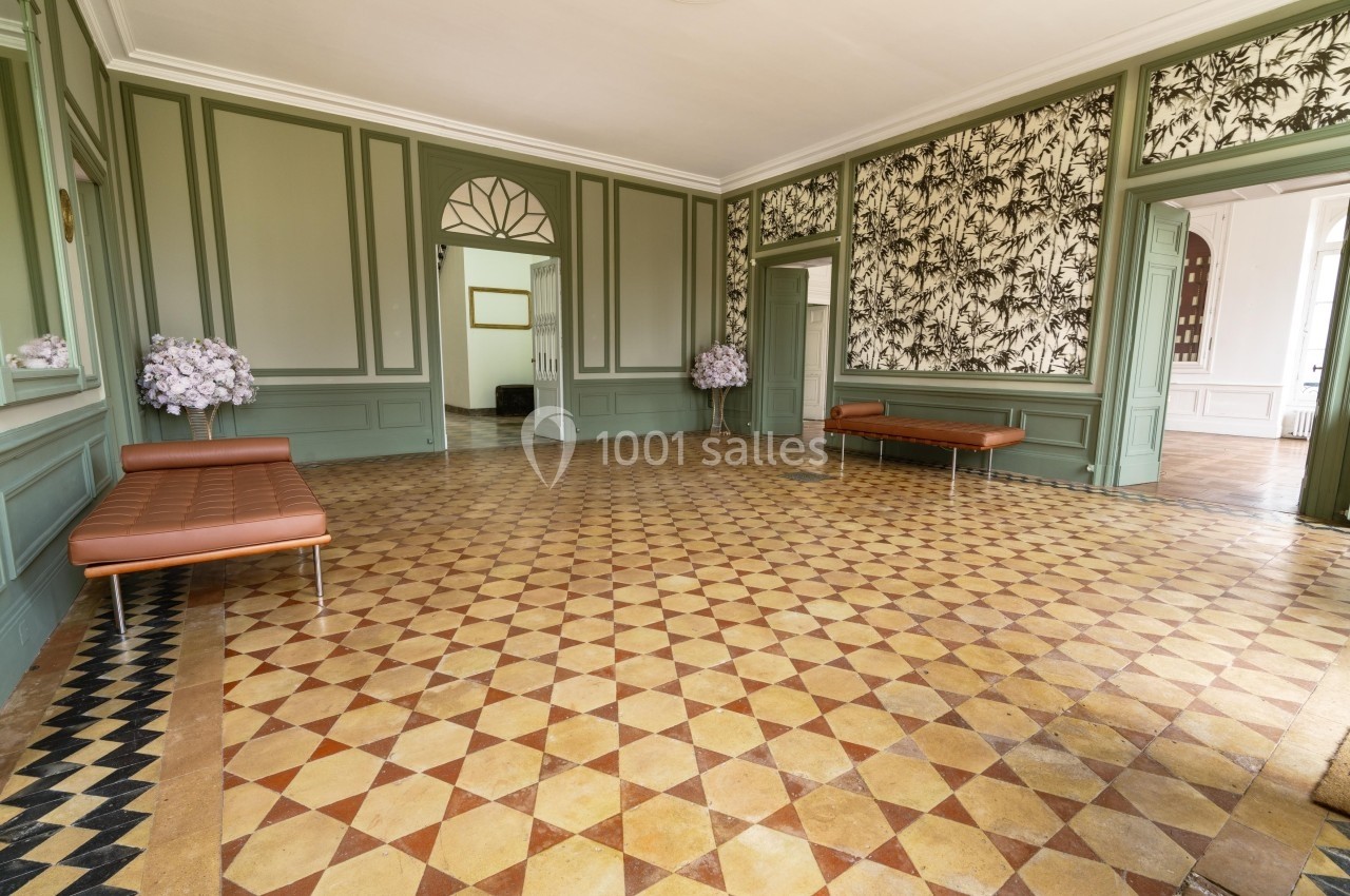 Salle lumineuse avec carrelage géométrique, murs verts, bancs en cuir et décorations florales aux angles.