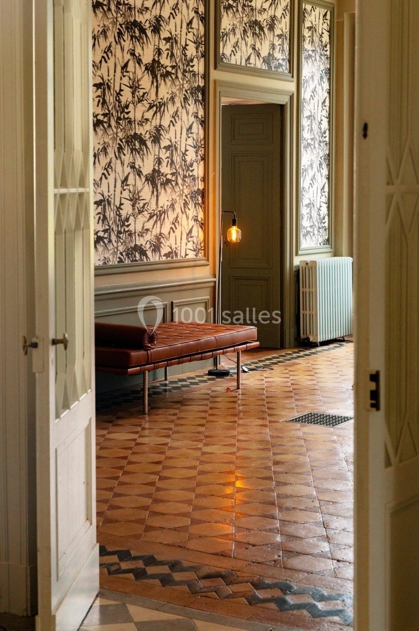 Vue d'un intérieur élégant avec un banc en cuir, un sol en carreaux anciens et un mur décoré de motifs végétaux.