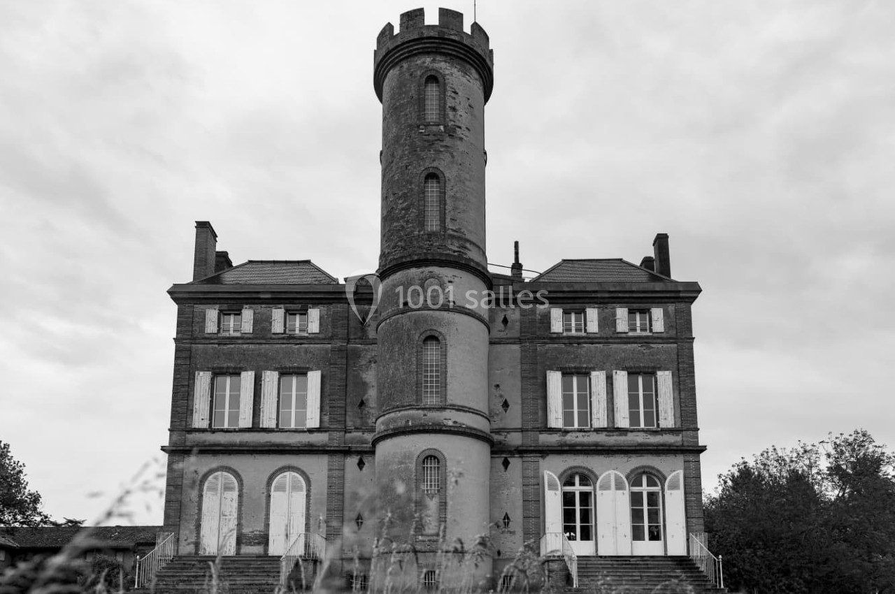 Façade d'un château ancien en briques avec une tour centrale ronde, sous un ciel nuageux.
