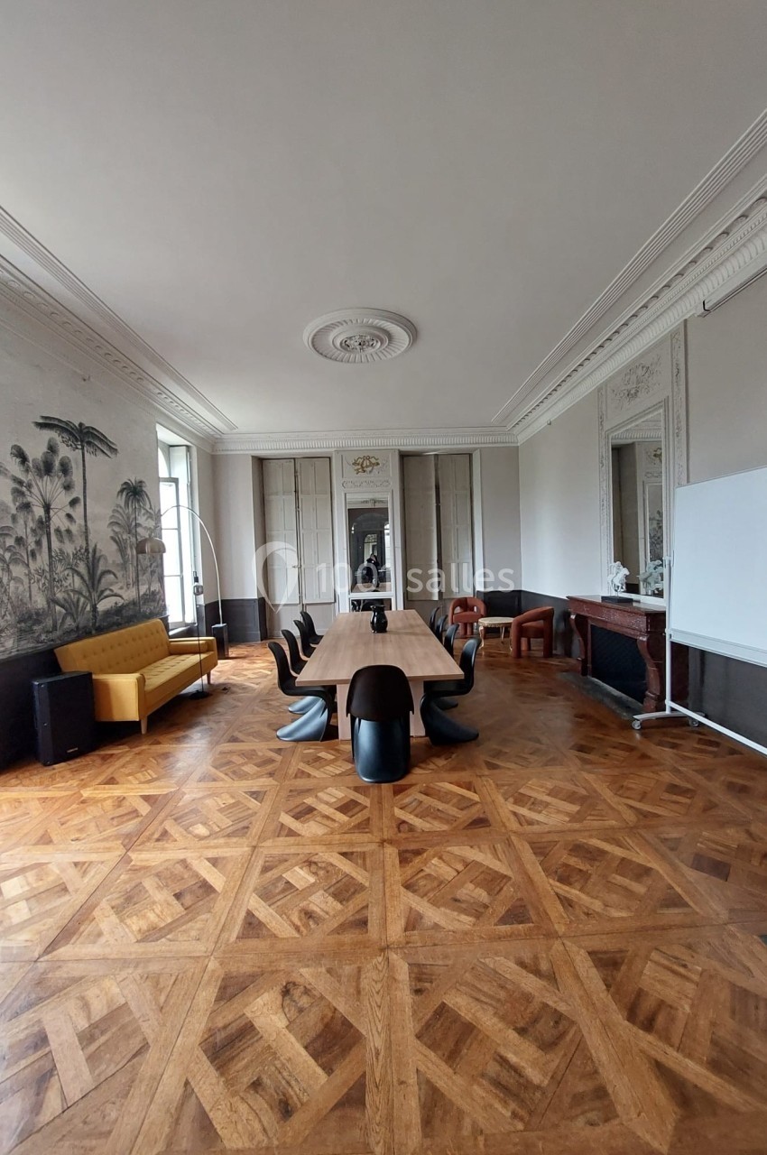 Salle de réunion élégante avec parquet en bois, table centrale, chaises noires, canapé jaune et fresque murale.