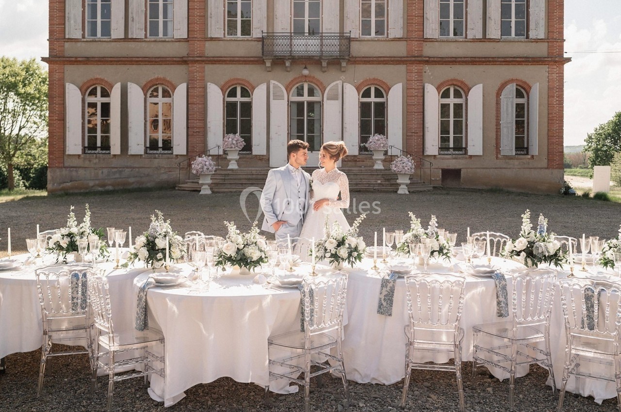 Un couple en tenue de mariage se tient devant une table élégamment dressée, avec un château en arrière-plan.