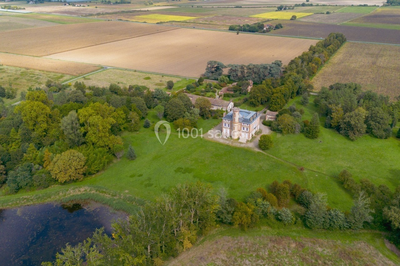 Vue aérienne d'une église entourée de verdure, avec des champs cultivés et un étang à proximité.