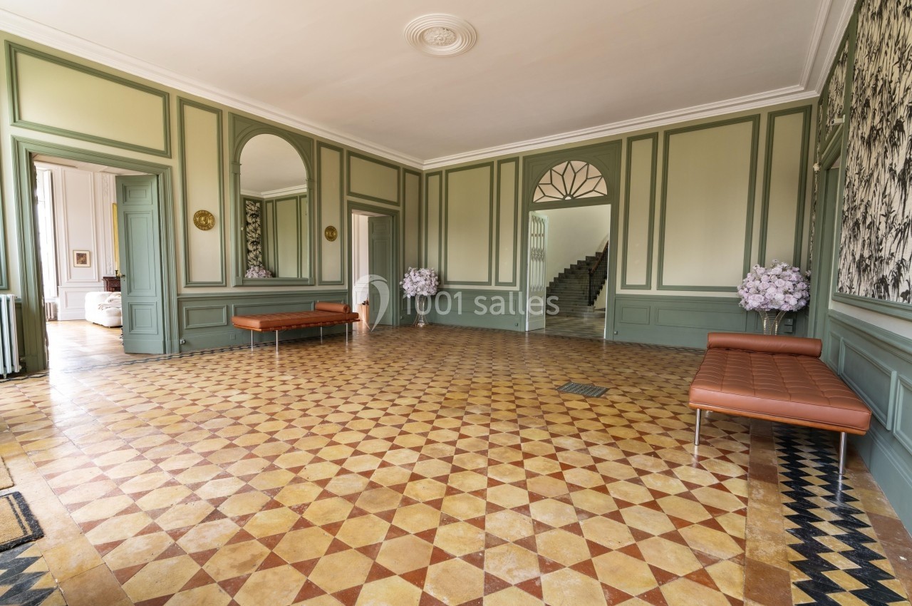 Salle lumineuse avec sol en carreaux géométriques, murs verts ornés de moulures et bancs en cuir marron.