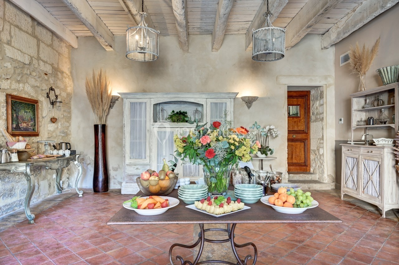 Salle à manger rustique avec table garnie de fruits et fleurs, entourée de meubles anciens et décorations champêtres.