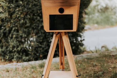 Appareil photo sur trépied en bois avec lampe circulaire, installé dans un jardin verdoyant.