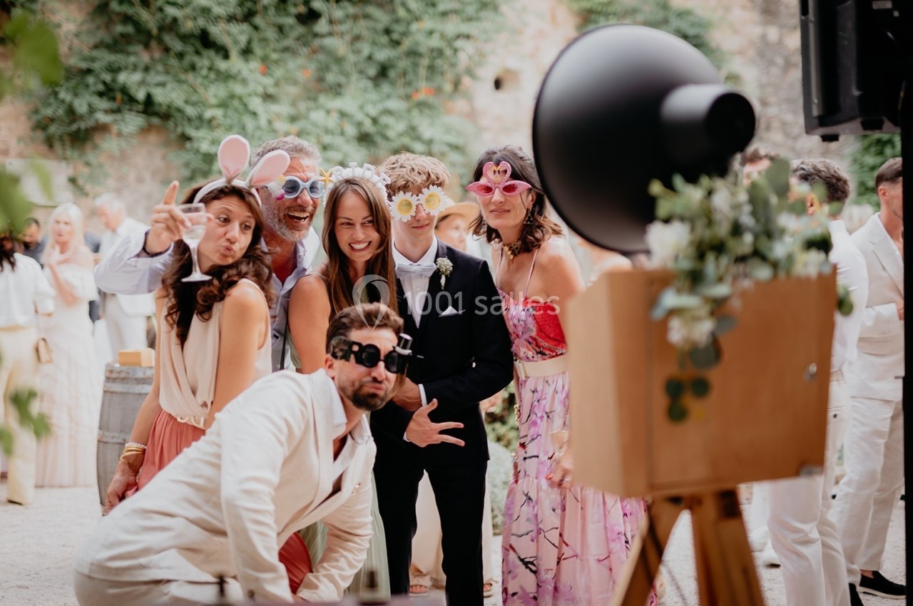 Des personnes déguisées avec des accessoires amusants posent devant un photobooth lors d'un événement en plein air.