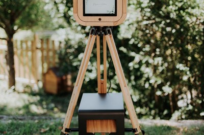 Miniature Lively Booth #6 Appareil photo en bois monté sur un trépied, installé dans un jardin avec des arbres en arrière-plan.