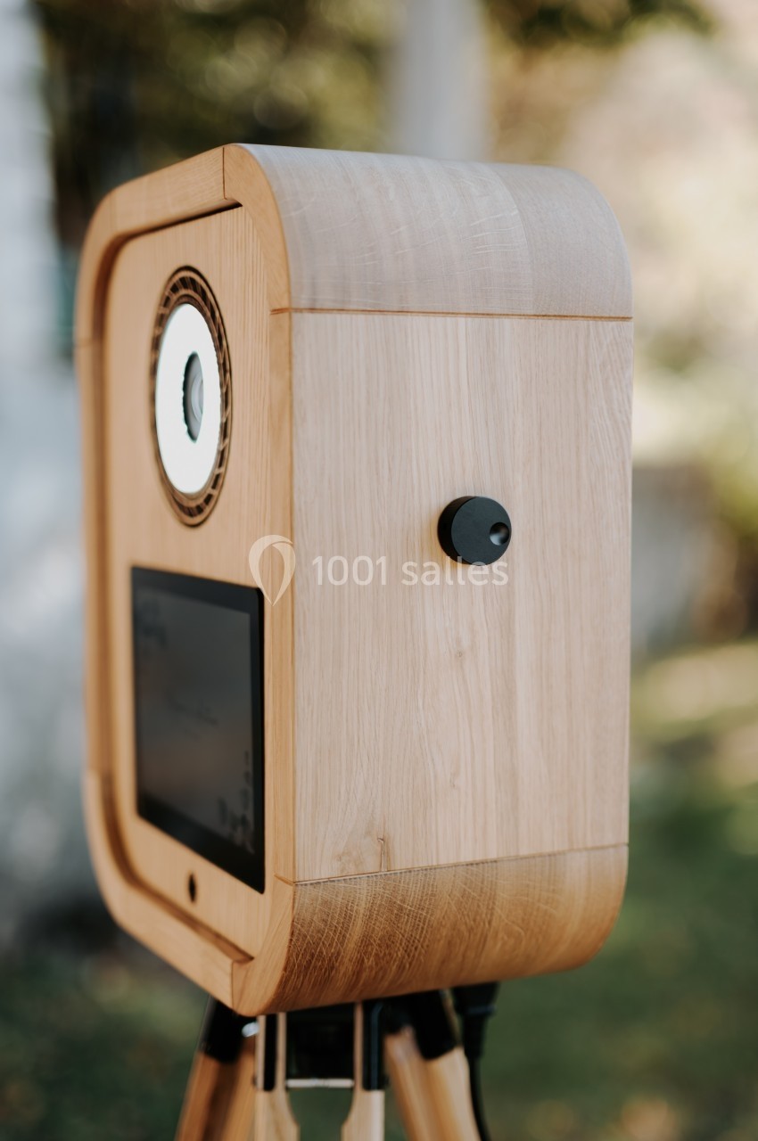 Boîtier en bois sur trépied avec un écran et un objectif circulaire, utilisé en extérieur.