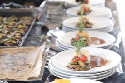 Miniature Traiteur Saint-Vallier-de-Thiey (Alpes-Maritimes) - Traiteur D'azur #6 Un cuisinier en tenue noire prépare des légumes dans une poêle en extérieur, devant un mur en pierre.
