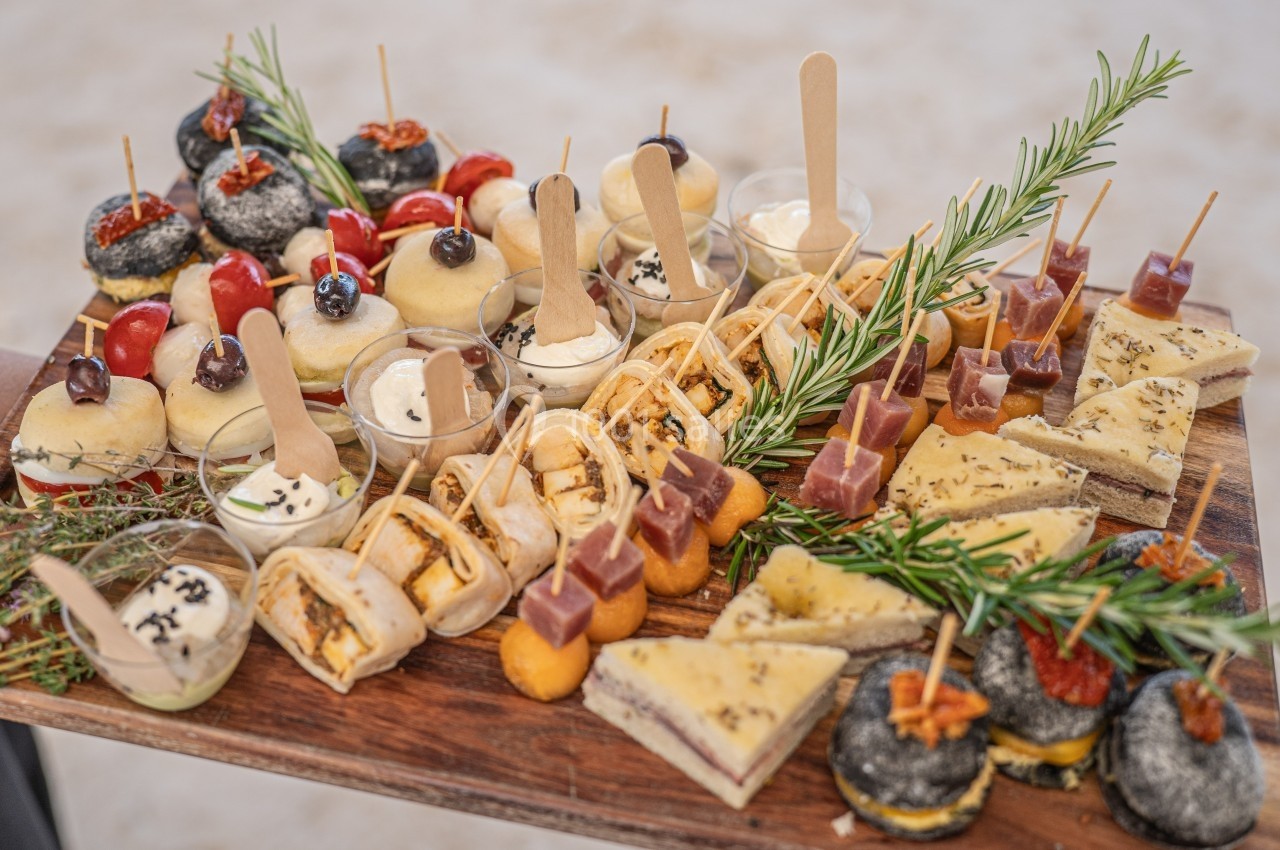 Plateau en bois garni de divers amuse-bouches salés et sucrés, décoré de branches de romarin.