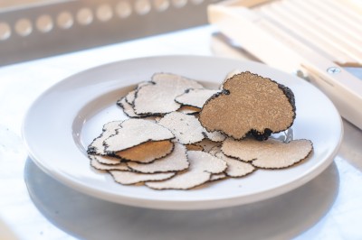 Miniature Traiteur Saint-Vallier-de-Thiey (Alpes-Maritimes) - Traiteur D'azur #8 Un cuisinier en tenue noire prépare des légumes dans une poêle en extérieur, devant un mur en pierre.