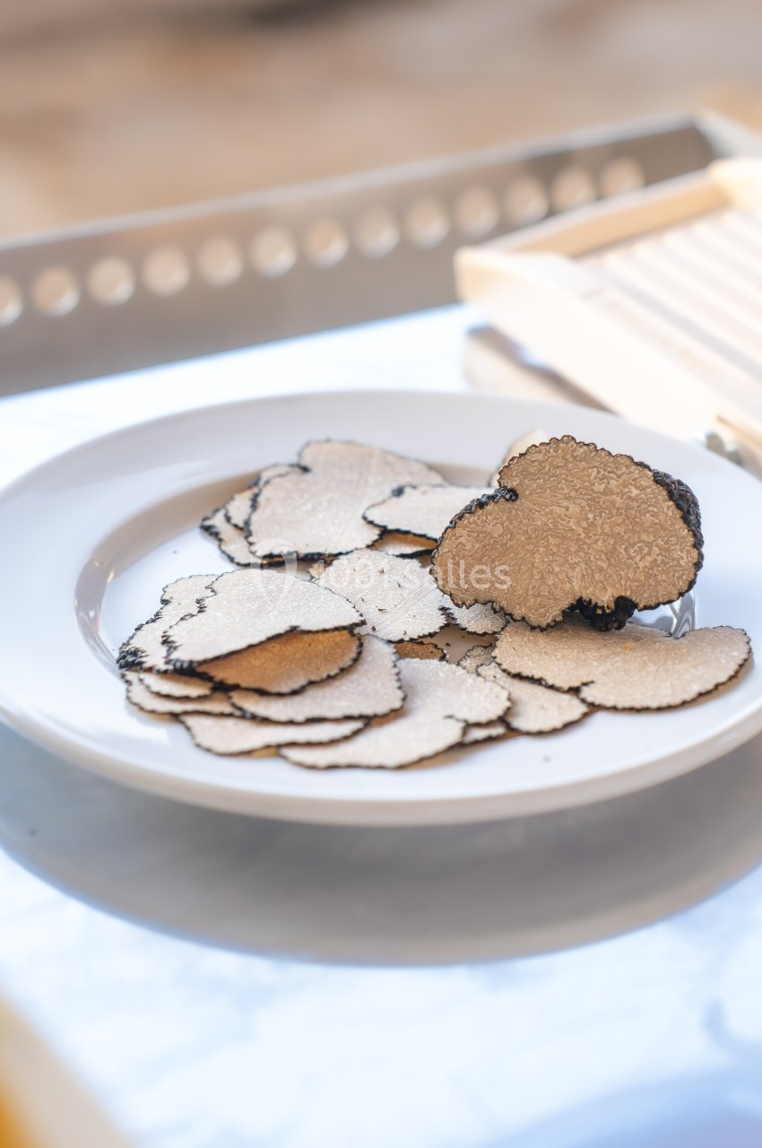Assiette de fines tranches de truffe noire posée sur une table lumineuse avec une mandoline en arrière-plan.