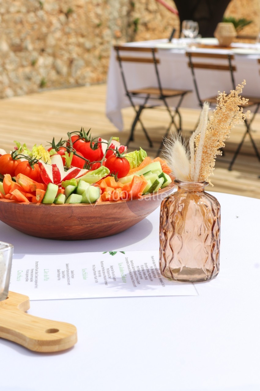 Salade de légumes frais dans un bol en bois sur une table dressée en extérieur avec un vase décoratif en premier plan.