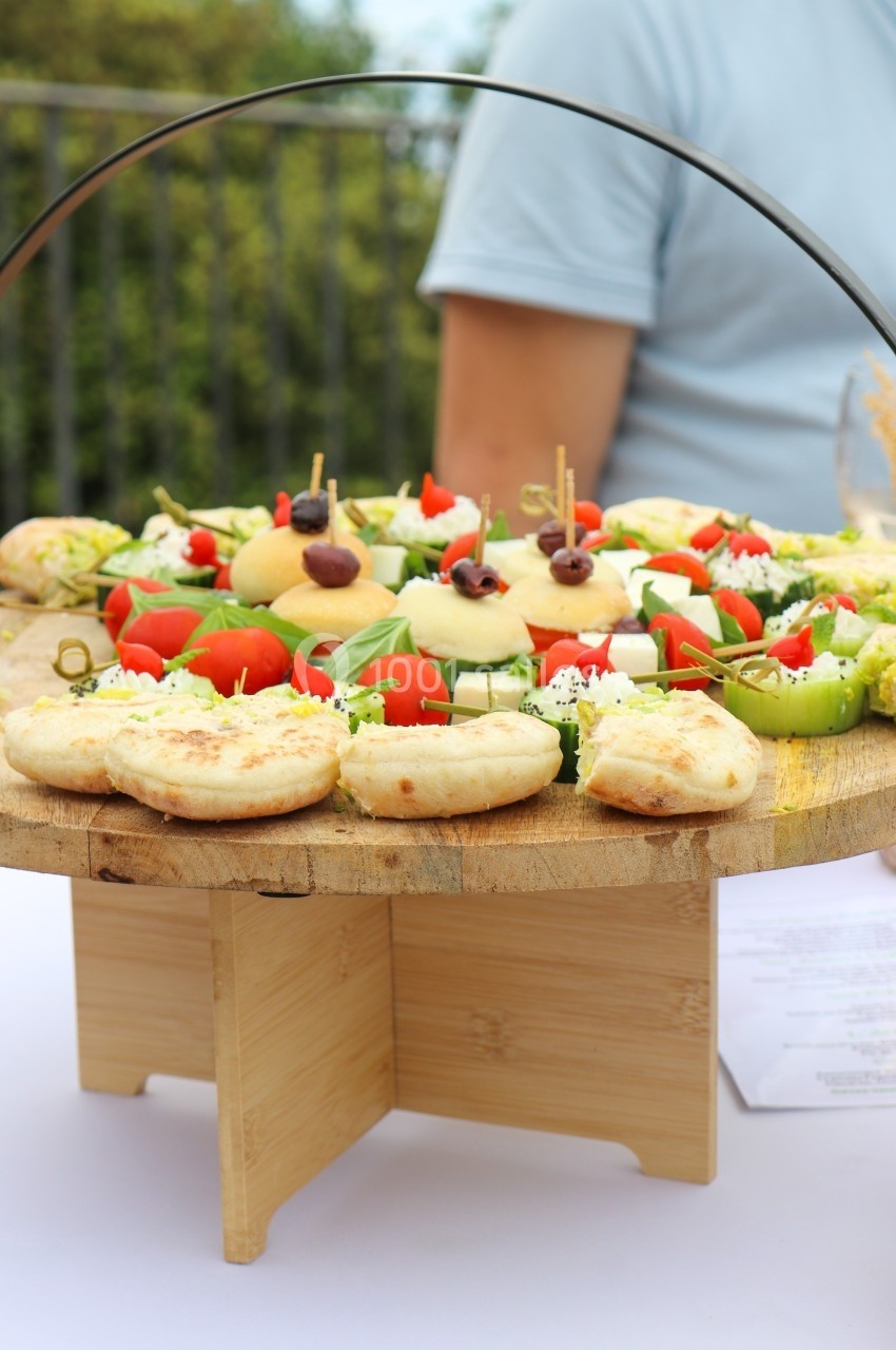 Plateau en bois garni de mini-sandwichs, légumes frais et amuse-bouches, présenté sur une table en extérieur.