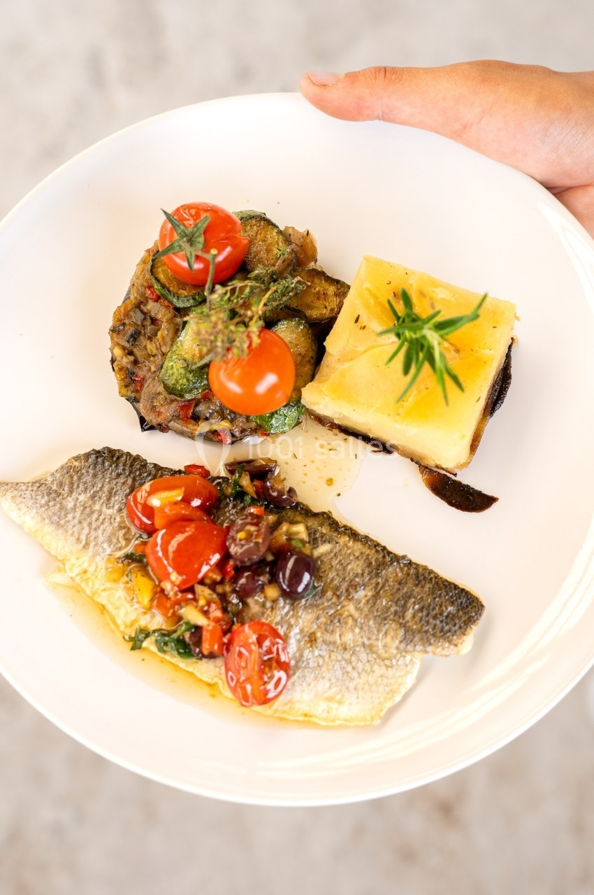Assiette contenant un filet de poisson, légumes grillés, tomates cerises et un gratin de pommes de terre.