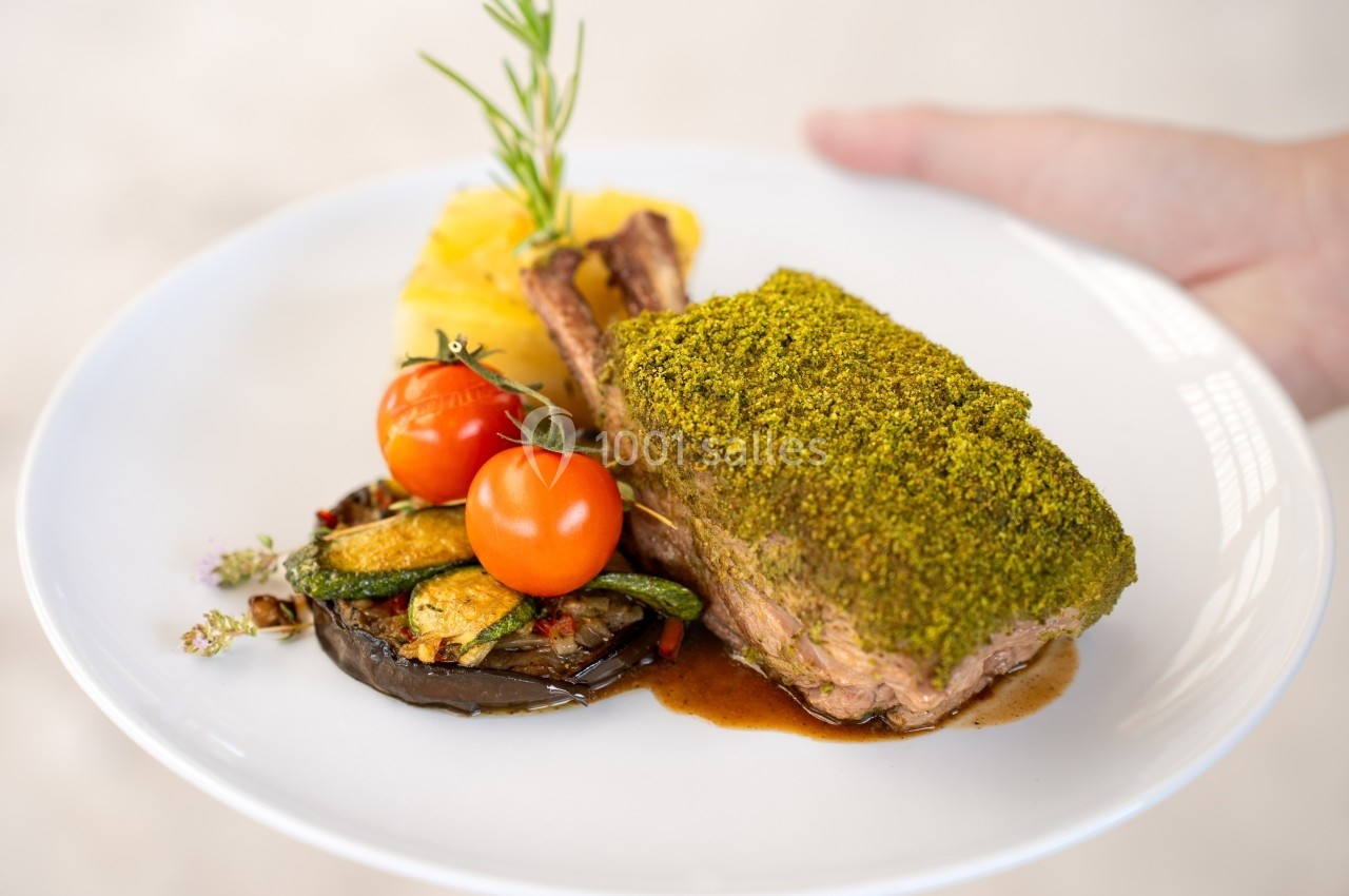 Carré d'agneau en croûte d'herbes servi avec légumes grillés, tomates cerises et gratin de pommes de terre.