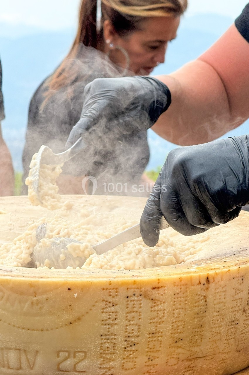 Préparation de risotto crémeux dans une meule de fromage, avec des mains gantées manipulant des ustensiles.