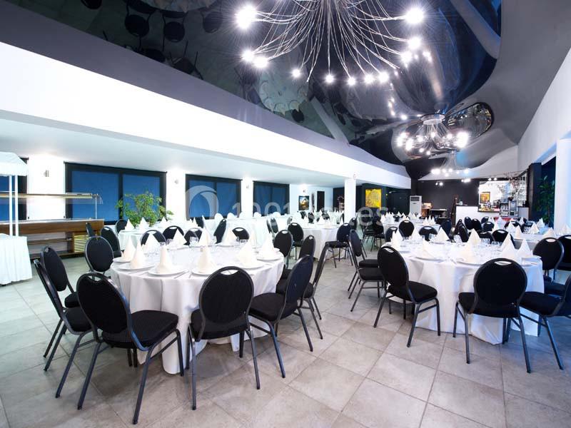 Salle de réception moderne avec tables rondes dressées, chaises noires et éclairage suspendu design.