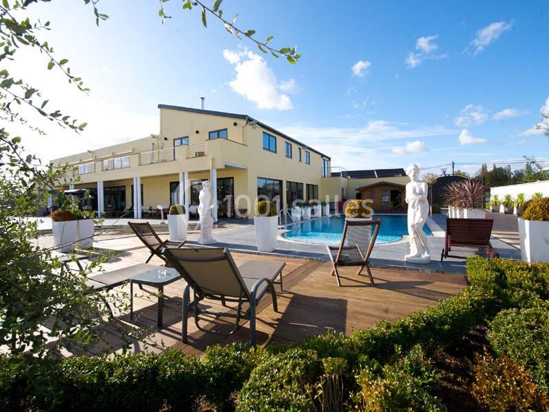 Vue d'une terrasse avec piscine, chaises longues, statues décoratives et un bâtiment moderne en arrière-plan.