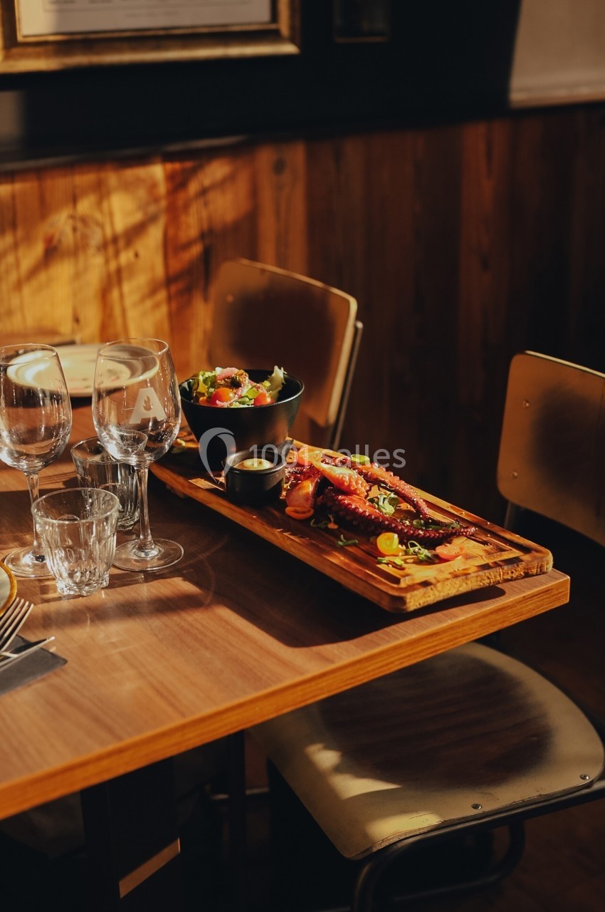 Plat de fruits de mer et salade servis sur une table en bois avec des verres et une lumière naturelle tamisée.