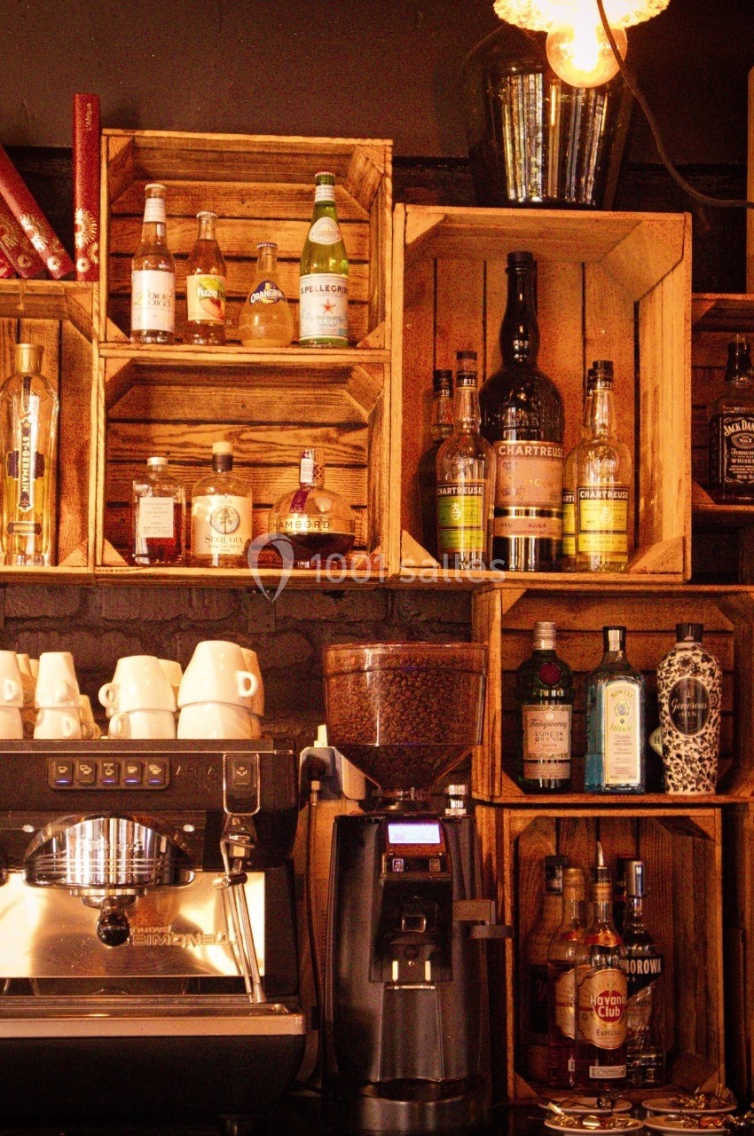 Étagères en bois remplies de bouteilles d'alcool derrière une machine à café et un moulin à café dans un bar.
