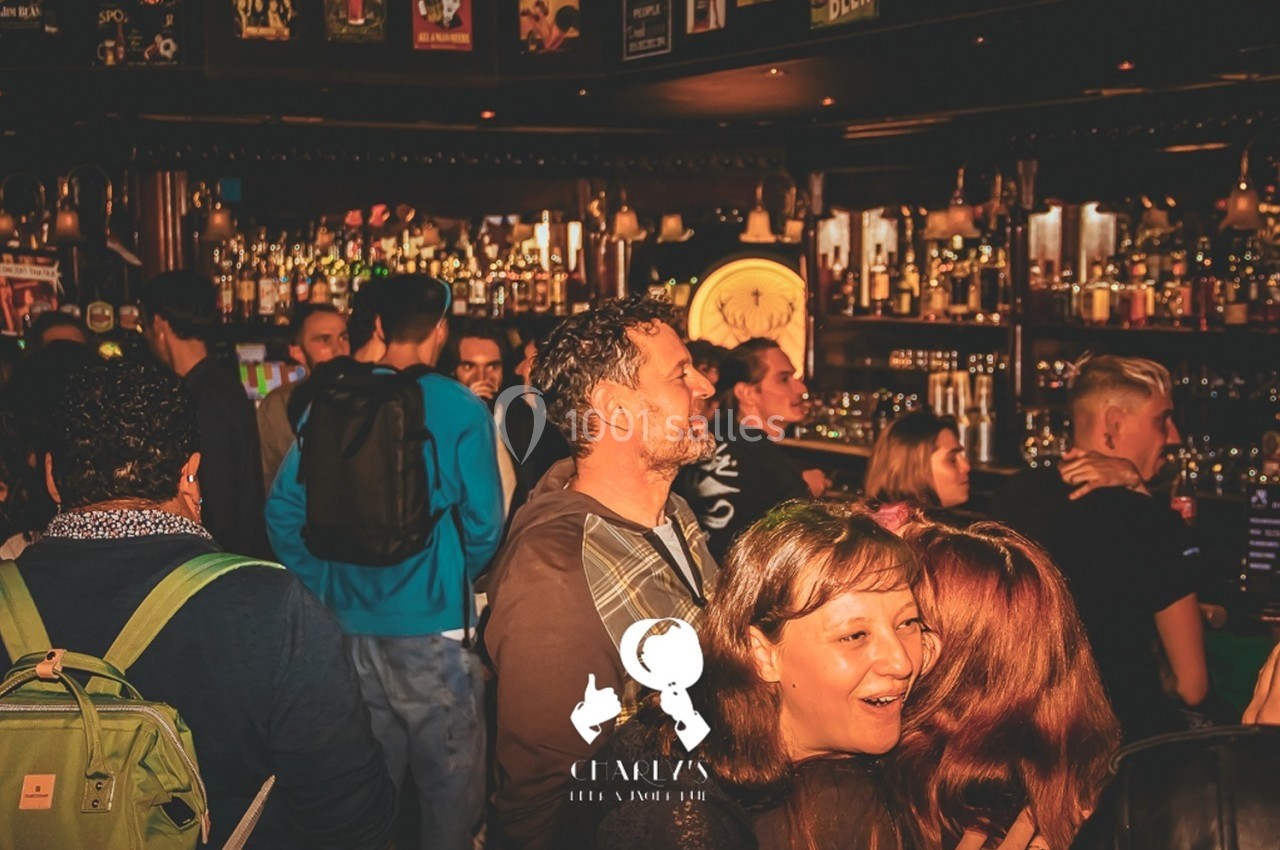 Des personnes discutent et s'amusent dans un bar animé, avec un comptoir rempli de bouteilles en arrière-plan.