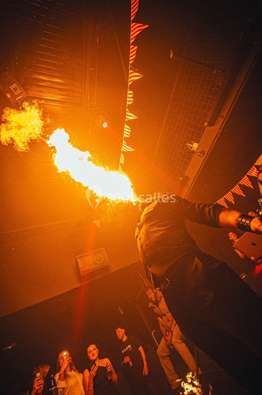 Un artiste cracheur de feu performe devant un public dans une ambiance sombre et festive.