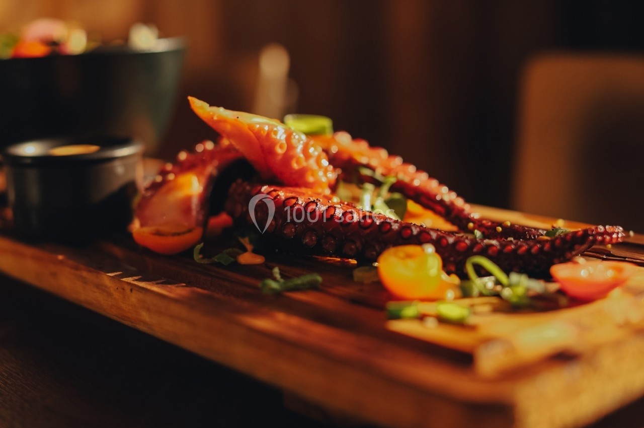 Tentacules de poulpe grillés servis sur une planche en bois avec légumes et herbes en garniture.