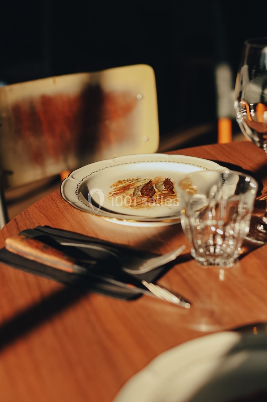 Assiette décorée posée sur une table en bois, accompagnée de couverts, d'un verre et d'une serviette noire.