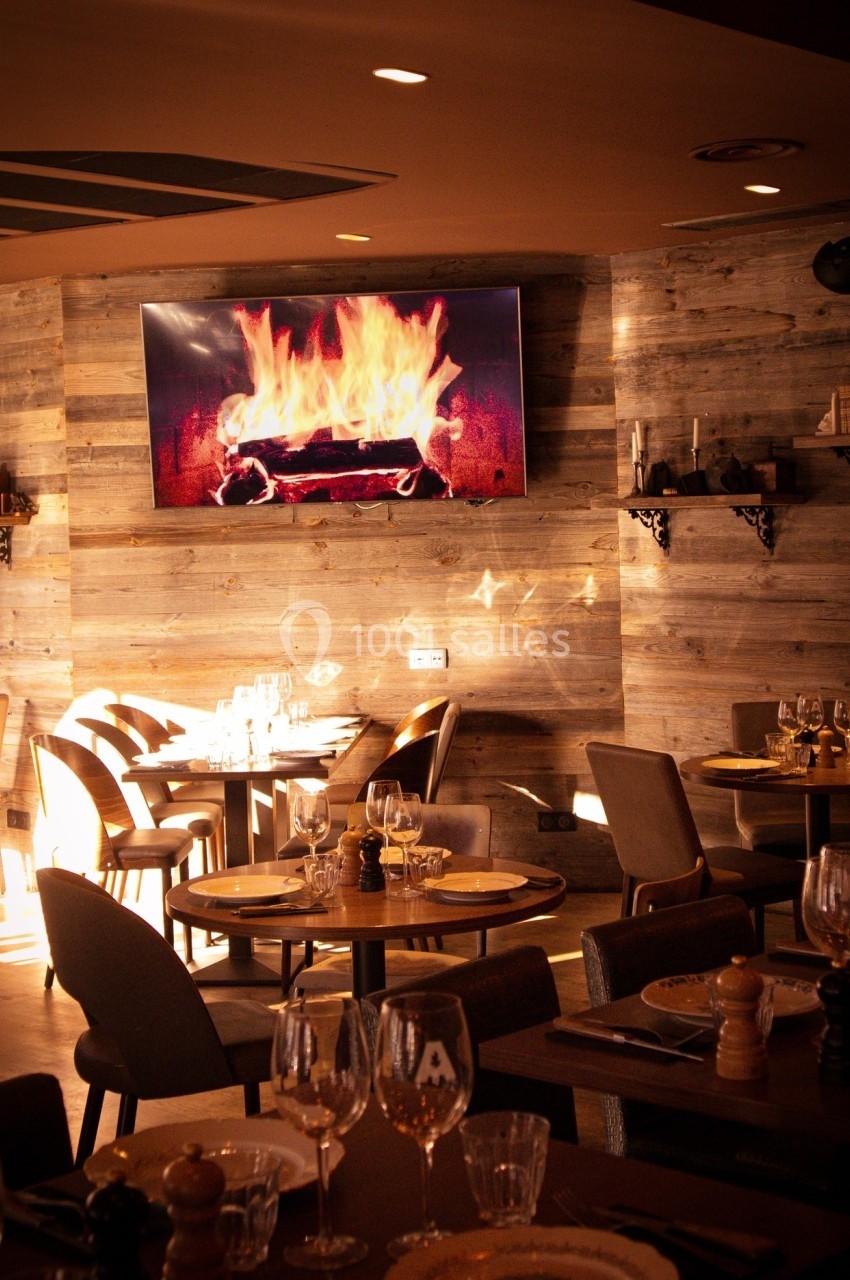 Salle de restaurant chaleureuse avec des tables dressées et un écran affichant une cheminée en feu.