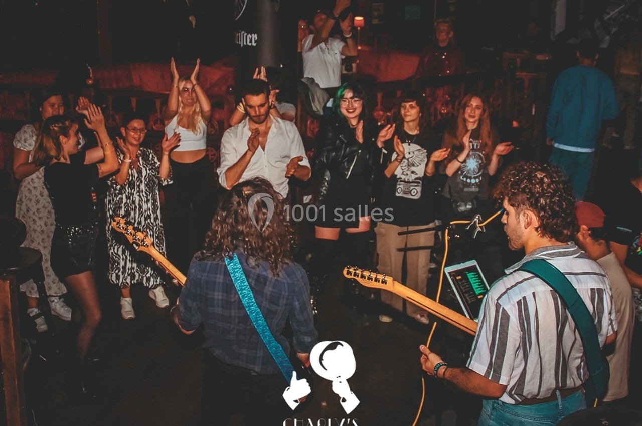 Musiciens jouant sur scène dans un bar, entourés d'un public debout applaudissant et dansant.