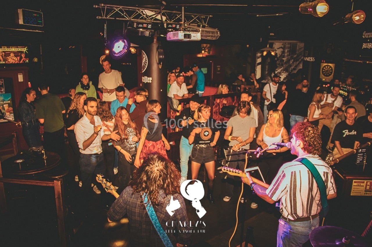 Un groupe de musiciens joue sur scène dans un bar animé, avec un public dansant et applaudissant.