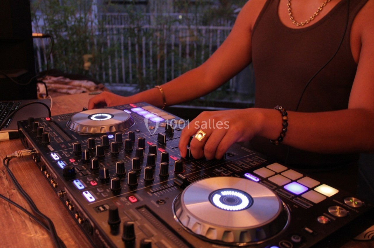 Un DJ mixe de la musique sur une console équipée de boutons et platines lumineuses.