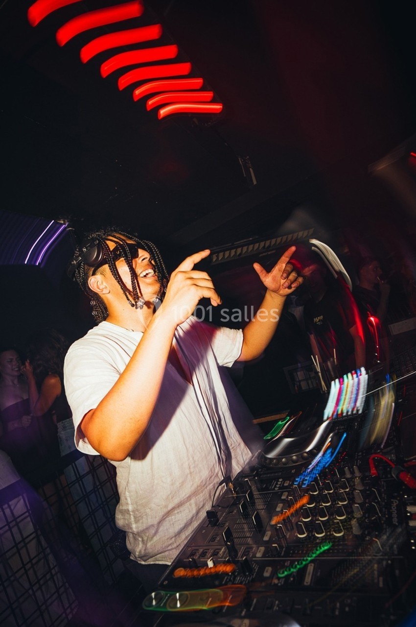 DJ mixant sur une table de mixage dans une ambiance de club avec des lumières colorées et un public en arrière-plan.