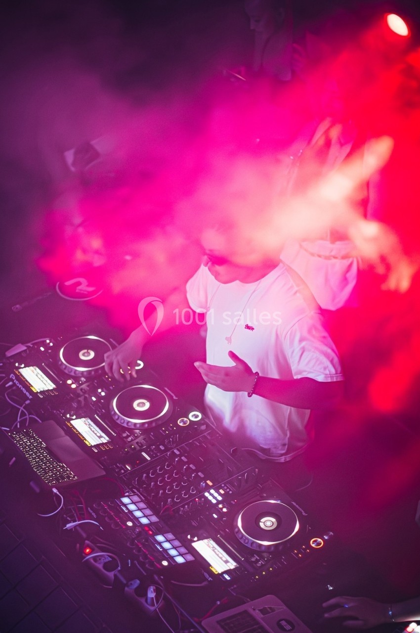 Un DJ mixe de la musique sur une table de mixage entourée de lumières rouges et de fumée.